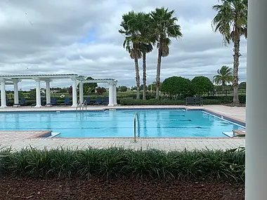 A community pool framed by a colonnaded pergola and a line of palm trees.