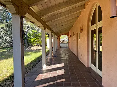 A covered loggia with terra cotta pavers running the length of a stucco courtyard home.