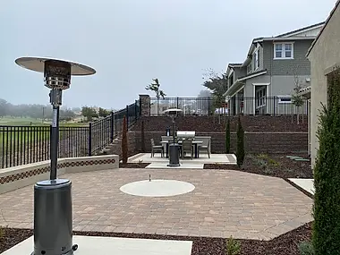 A paver patio steps down toward a retaining-wall dining nook, with the home rising behind it.