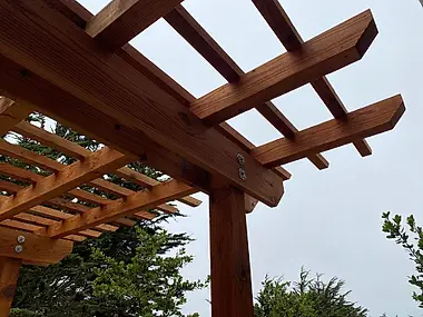Close-up of a pergola's cedar beam joinery, bolted and finished for years outdoors.