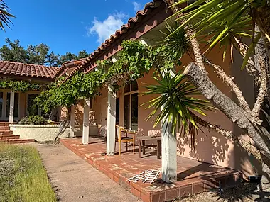 A vine-draped porch along a tile-roofed hacienda, its columns wrapped in climbing greenery.