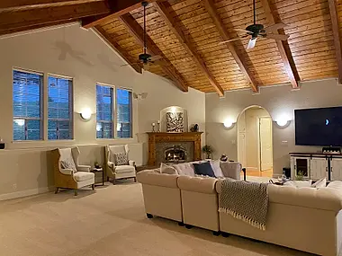 A great room with an exposed wood-beam ceiling, a stone fireplace, and a pair of wingback chairs.