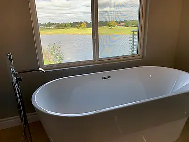 A freestanding soaking tub positioned for a water view through the bathroom window.
