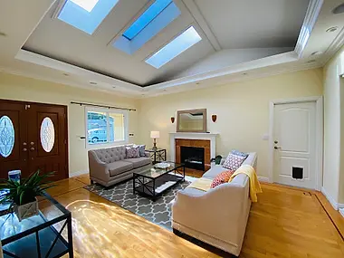 Sun-washed living room with a vaulted, skylit ceiling and a pair of tufted sofas around the fireplace.