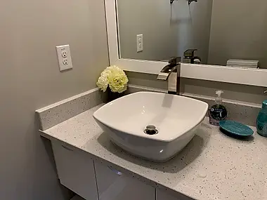 A vessel sink and waterfall faucet set into a speckled quartz vanity.