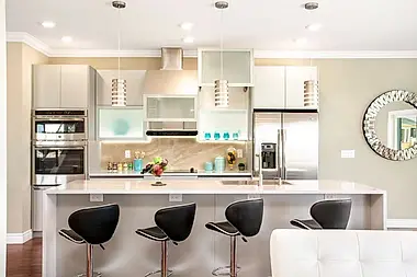 A crisp white kitchen with glass-front cabinets, a trio of drum pendants, and a full stainless suite.